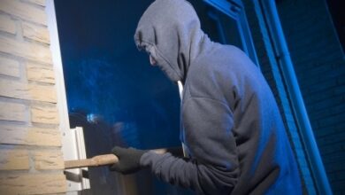 Persoon probeert in het donker met een breekijzer een raam open te wrikken, symbool voor woninginbraak en veiligheid.